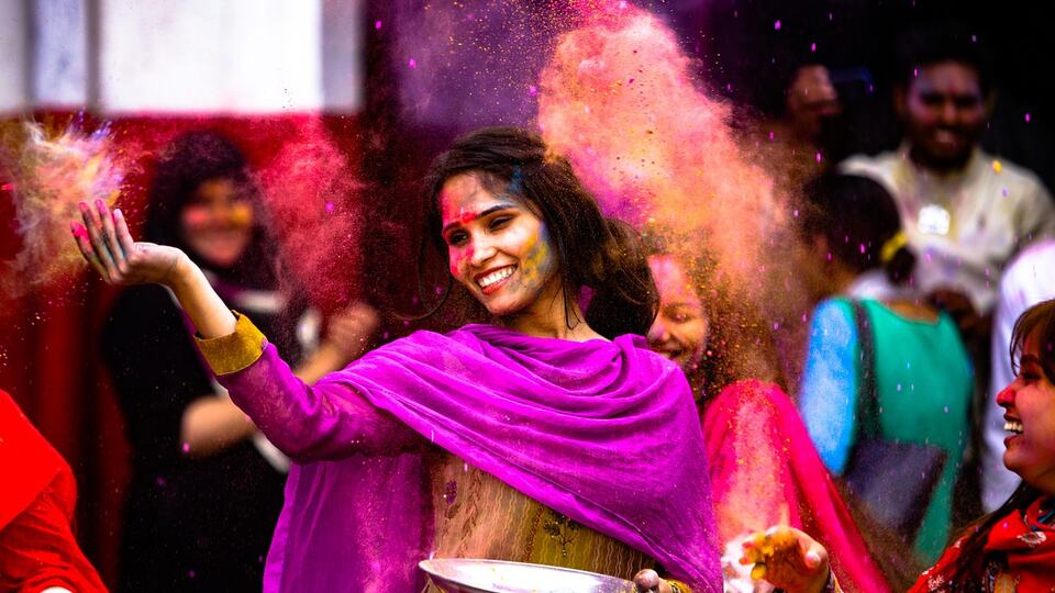 Young woman dancing in a cloud of coloured powder during the Holi festival in India