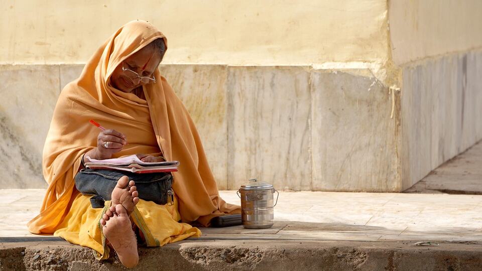 Woman in an orange sari sitting on stone steps in India