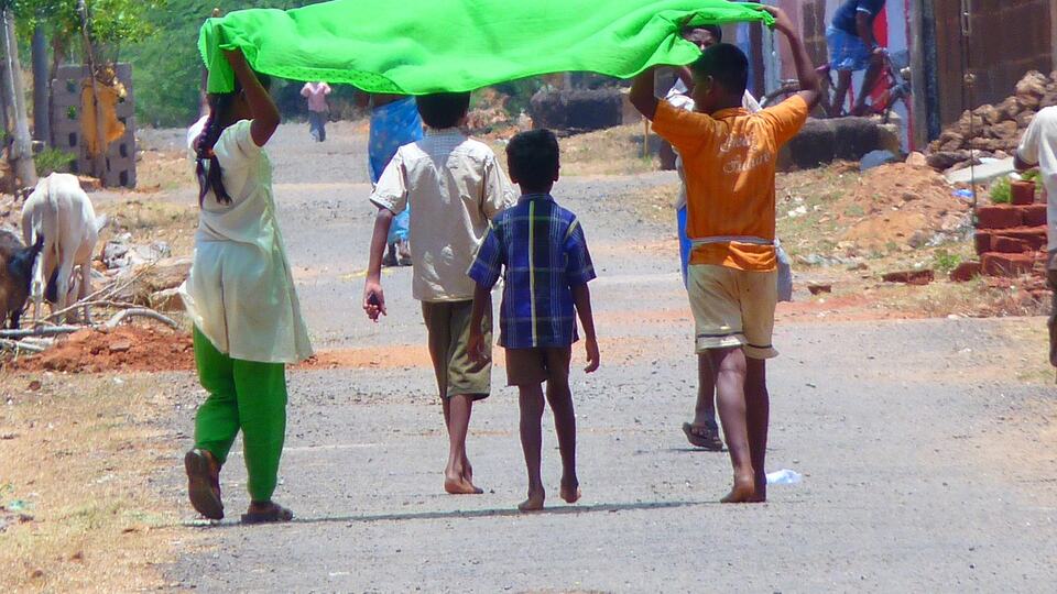 Children shading themselves from the summer sun with a cloth on an Indian road