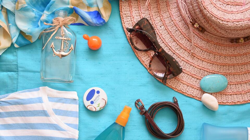 Straw sun hat, sunscreen and sunglasses laid out for a beach holiday